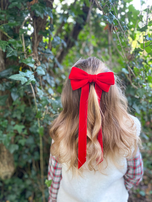 Little Love 'Ever After' velvet bow hair clip in true red, red velvet hair bow for with red bow worn by girl with tartan dress and cream fur gilet beside ivy in woodland