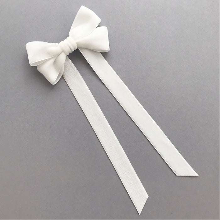 An ivory velvet hair bow with two long ribbon tails, displayed on a neutral gray background.