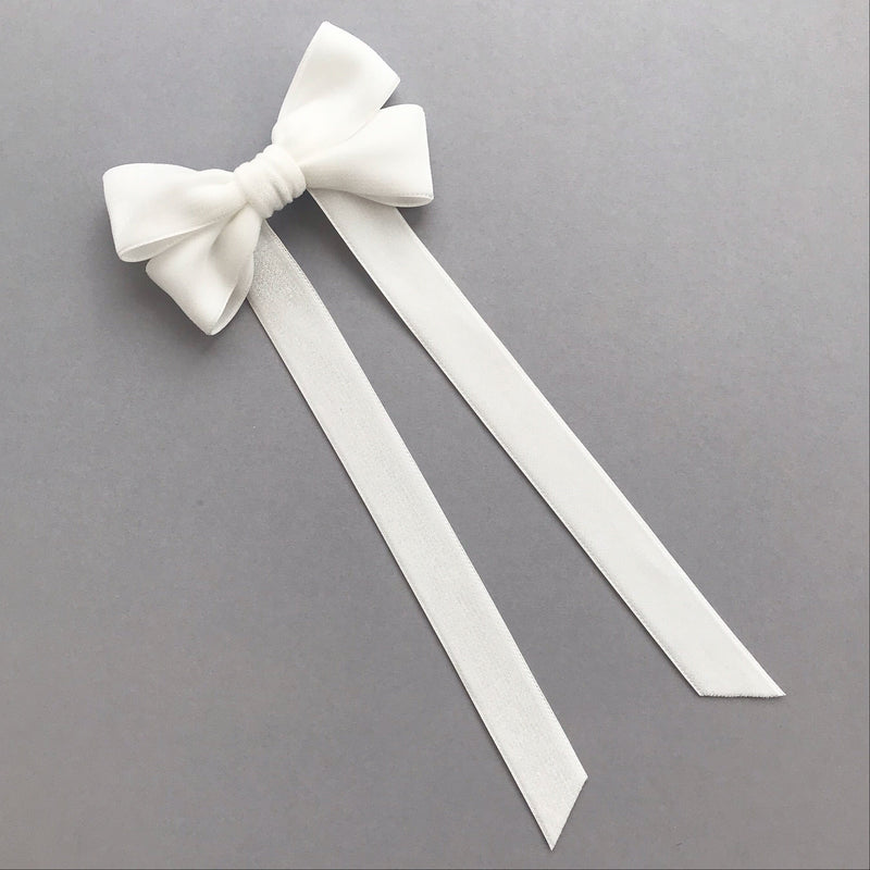 An ivory velvet hair bow with two long ribbon tails, displayed on a neutral gray background.